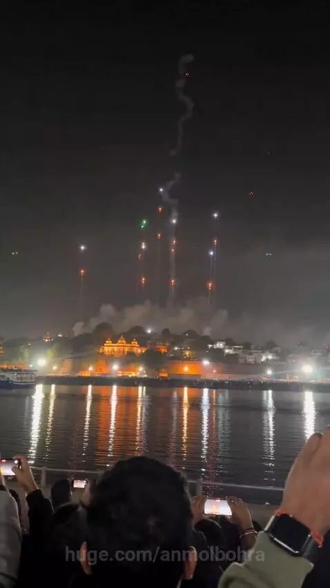 Nighttime light show depicting Lord Murugan with a trident and peacock, reflected on water, with fireworks.