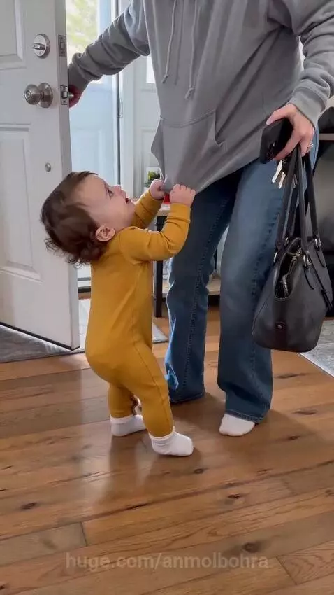 Baby in yellow romper holding onto mom's shirt, looking sad, then smiling.