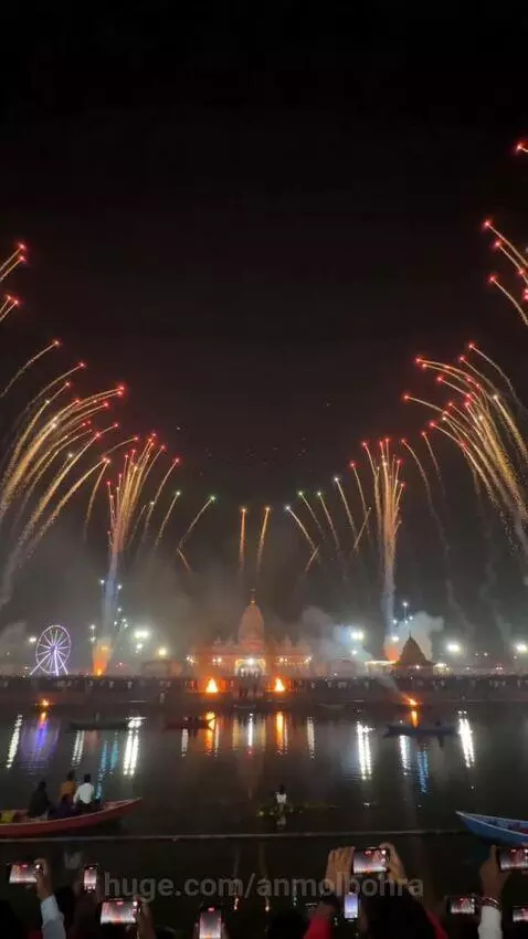 Drone light show forming Lord Krishna image with fireworks over water at night, temple in background.