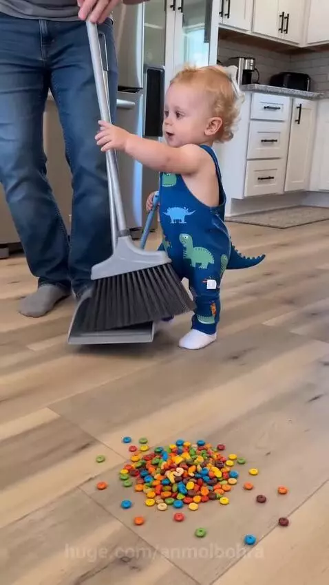 Dad and baby with brooms in a kitchen, baby attempts to sweep candies.