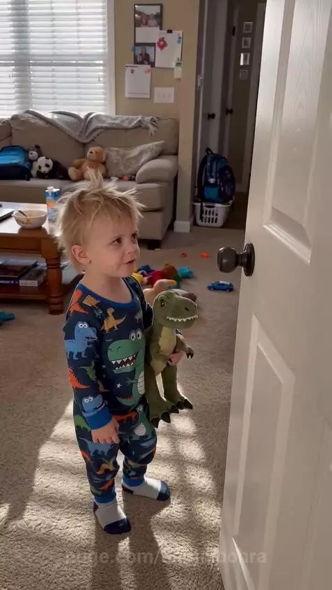 Toddler in dinosaur pajamas confronts dad peeking from behind a door about watching funny videos.