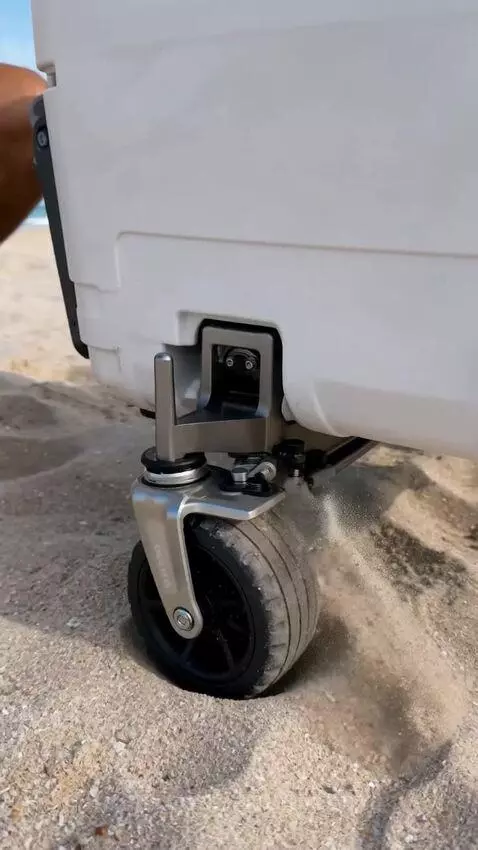 White cooler transforming into a motorized beach trike with large wheels on a sandy beach.