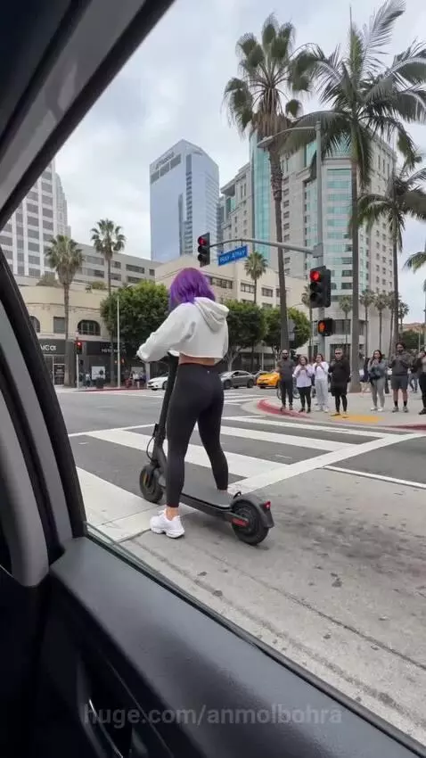 Woman on an electric scooter that transforms into a three-wheeled enclosed commuter pod at a city intersection.