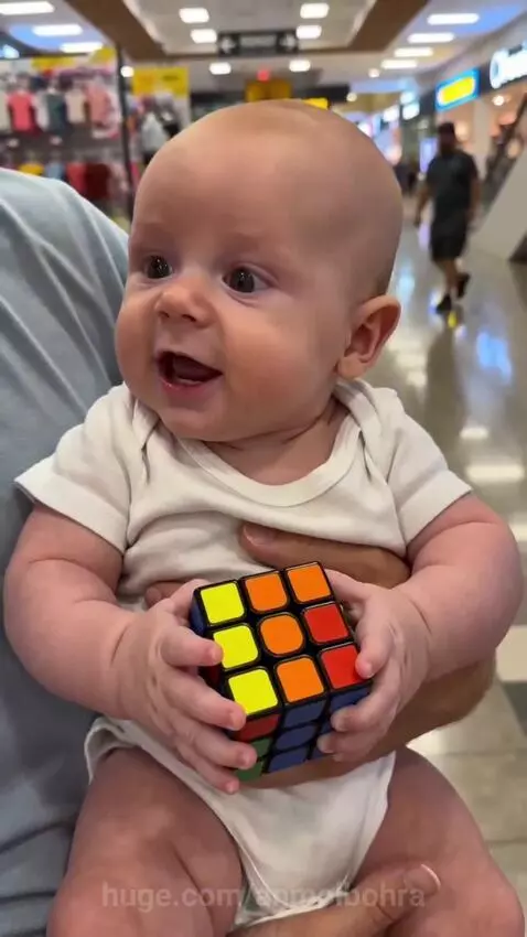 Baby holding a solved Rubik's Cube with a thumbs-up, looking surprised.
