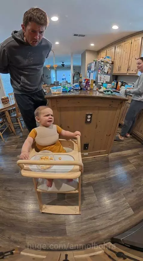Baby in high chair points accusingly at dad eating a snack, demanding it back.