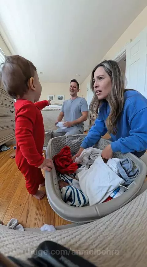 Baby in red onesie crying and pointing at dad while mom holds up a red sock.