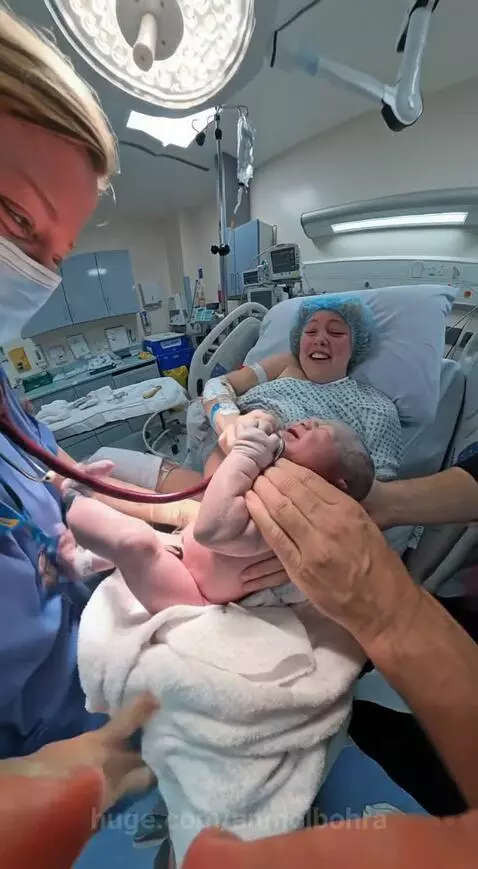 Newborn baby wrapped in a blanket playfully holding a doctor's stethoscope.