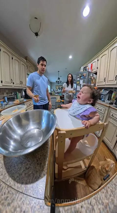 Father playfully bangs spoon on bowl, baby in high chair cries 'No!' and takes spoon.