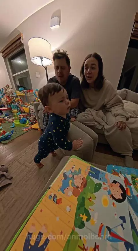 Baby in blue pajamas with yellow stars holding furniture, parents behind, surrounded by toys, saying 'No bed!'