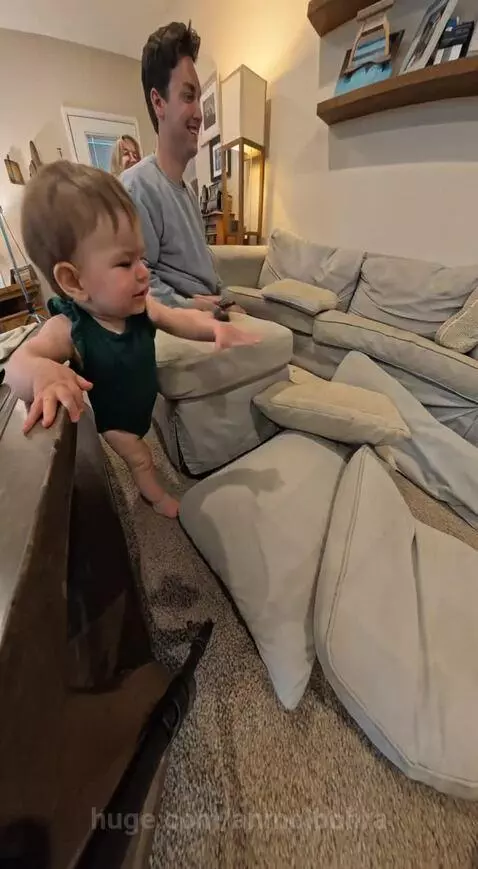 Baby looking at dad who is searching couch cushions for a remote control.