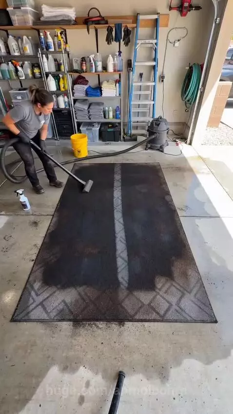 A very dirty rectangular rug being cleaned in a garage, showing a dramatic before and after transformation.