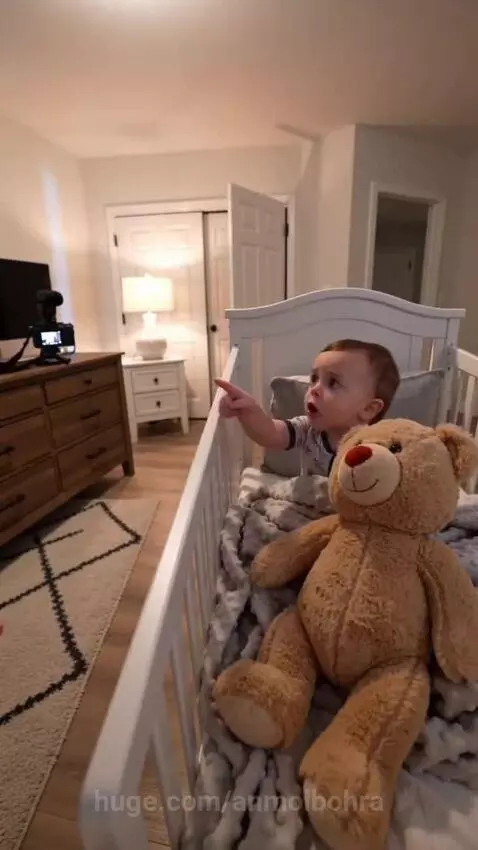 Baby points at teddy bear, demanding a goodnight kiss from mom.
