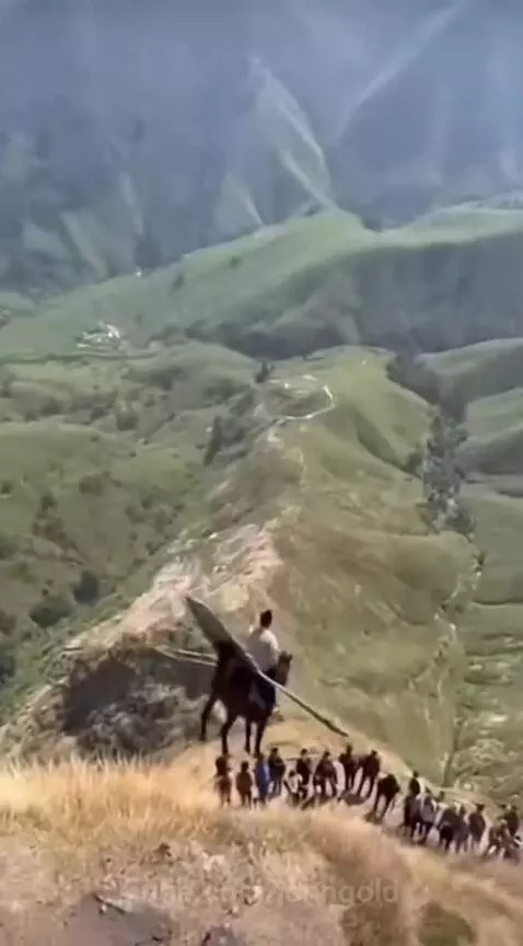 Man riding a blue-winged horse off a grassy cliff into a green valley, with cheering spectators below.