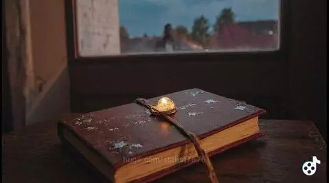 Close-up of an old, reddish-brown book with star patterns and a glowing orb on a wooden table.