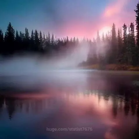Tranquil lake at sunset with vibrant sky colors reflecting on the water and mist.