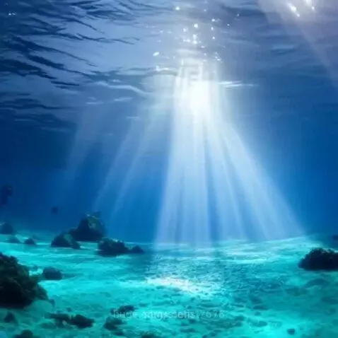 Sunlight rays illuminating a clear blue underwater scene with coral and rocks on a sandy seabed.