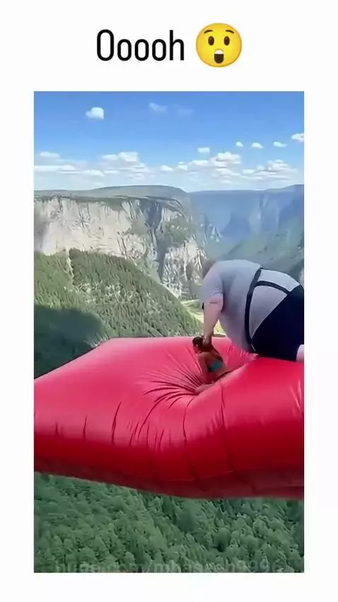 Man pushing woman on inflatable cushion towards a safety net suspended over a canyon.