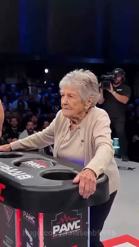 Elderly woman with arm raised in victory after winning a slap fight competition.