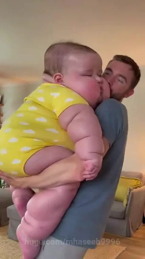 Bearded man holding a large baby wearing a yellow cloud onesie, patting its back to help it burp.