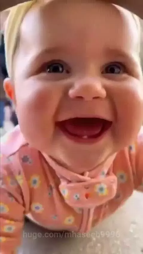 A baby gorilla approaches a glass enclosure where a human baby in a pink outfit is crawling and laughing.