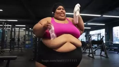 Woman in pink sports bra and black shorts wiping sweat with a towel and drinking water in a gym.