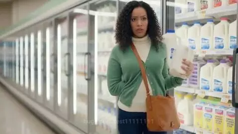 Woman in grocery store dairy aisle, holding milk jugs, with her chest unnaturally expanding.
