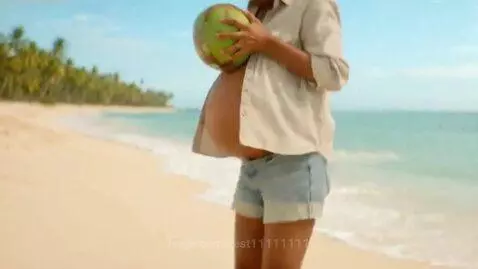 Woman on a sunny beach with a rapidly expanding, enormous, spherical belly after picking up a green coconut.