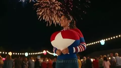 Latina woman in a red, white, and blue sweater celebrating Fourth of July at night with fireworks and string lights.