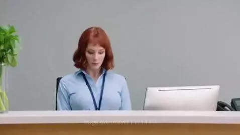 Woman with red hair at a reception desk, looking shocked as her chest inflates to an enormous size.