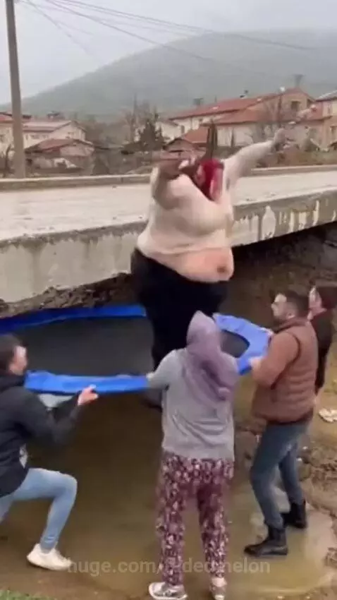 Woman in headscarf falling into muddy water after missing a trampoline jump.