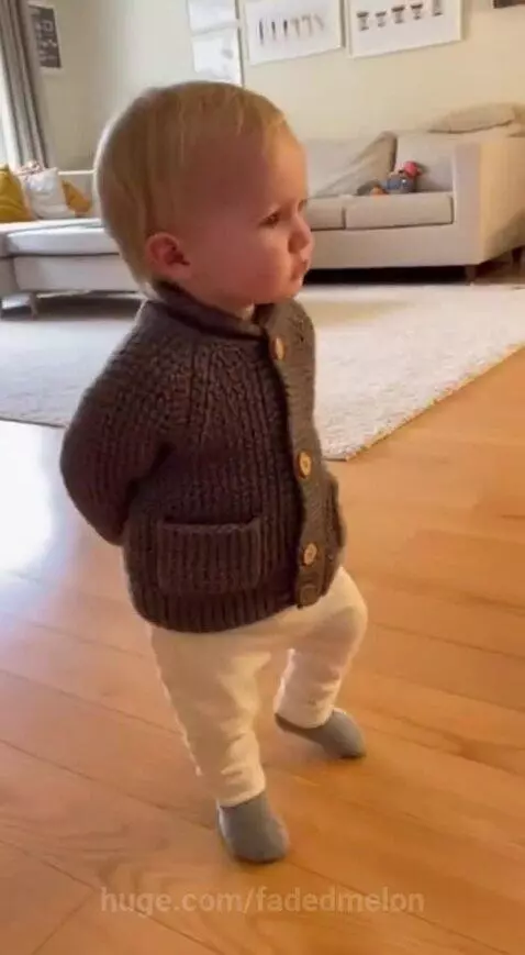 Toddler in a grey cardigan stands on a wooden floor, humorously replying 'Shut up, I'm Grandpa.'