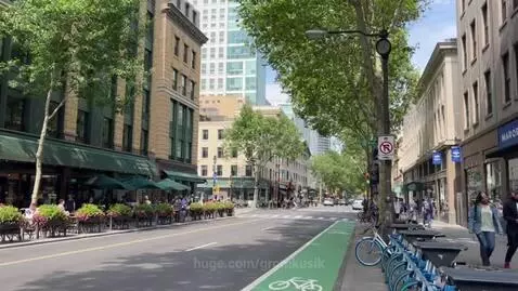 Wide shot of a sunny city street with a cafe, traffic, bike lane, and pedestrians.