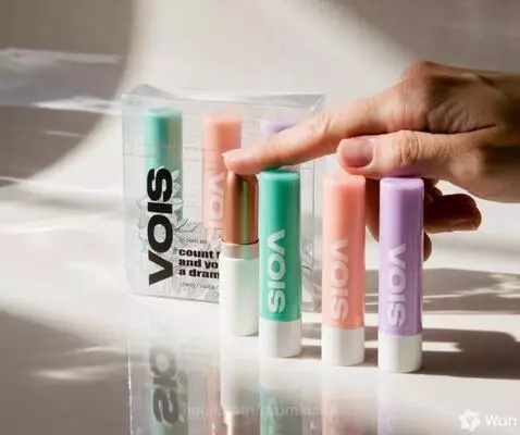 Close-up of a hand revealing a 'vois' lip balm set with three colorful lip balms and a bronze lipstick case.