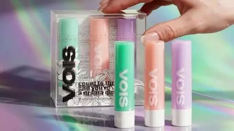 Close-up of a hand selecting a pastel green VOIS lip balm from a clear box.
