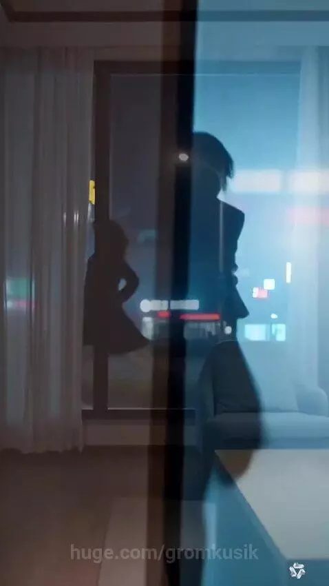 Nighttime city view from a window, showing a silhouette walking past under a streetlamp, with interior reflections.