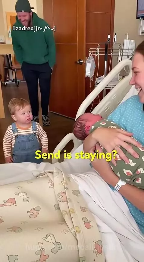 Toddler looking shocked and upset at a new baby sibling, with parents present.