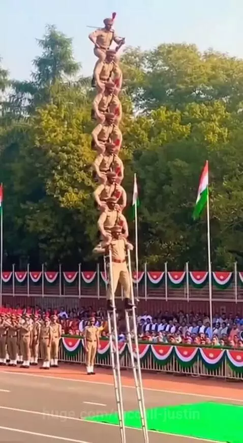 Men in uniform on stilts attempt a tall human pyramid during a parade, then it collapses.