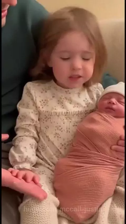 Young girl with light brown hair holding a newborn baby, showing immense love and tenderness.