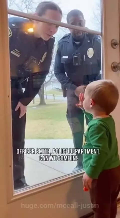 Young child in green shirt looking through glass door at police officers outside.