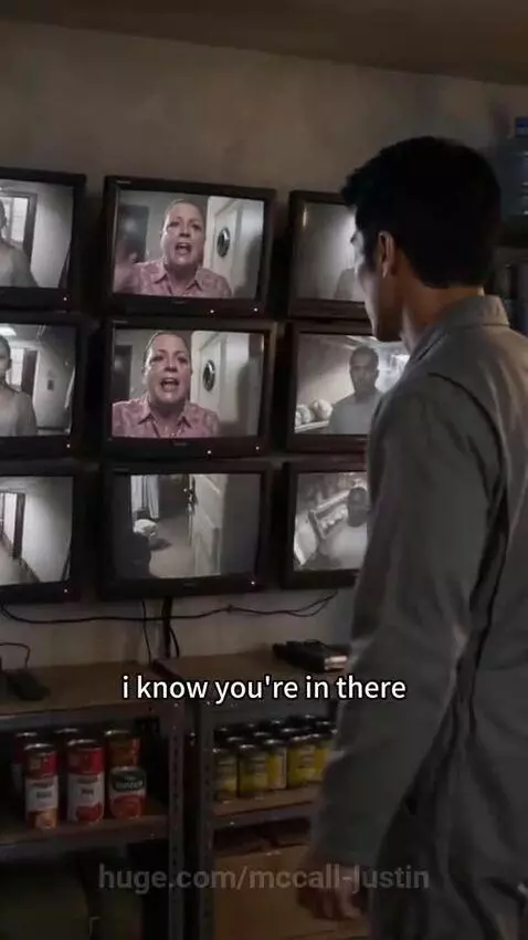 Man in a bunker with monitors watches a woman crying outside a metal door, pleading for help.