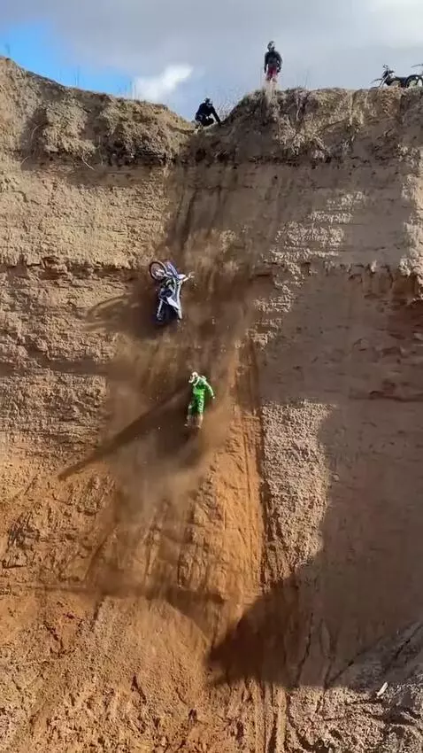 Dirt bike rider attempts a steep, dusty hill climb and crashes, tumbling down.