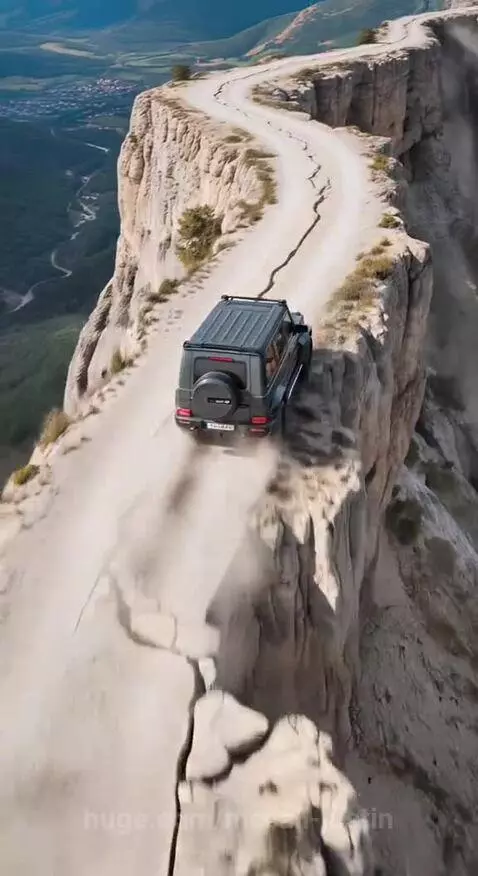 Dark grey Mercedes G-Wagen driving on a narrow dirt road along a steep cliff edge with dust billowing.