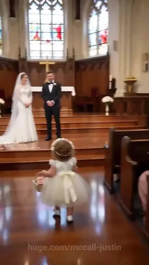 Flower girl in white dress and crown stops wedding procession to ask groom about bride's favorite snack.