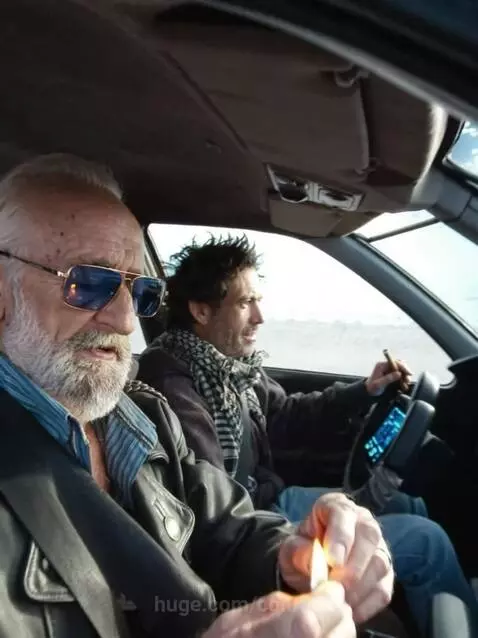 Man lighting cigar in a car that transforms into a spaceship hovering near a spiral galaxy.