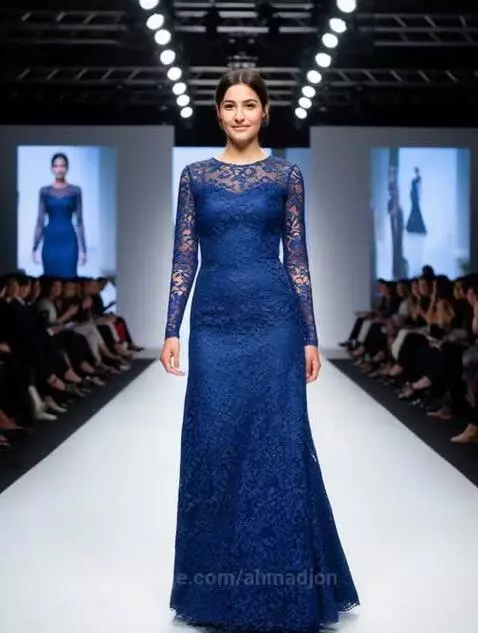 Model wearing a long, form-fitting royal blue lace gown with long sleeves and an open back on a fashion runway.