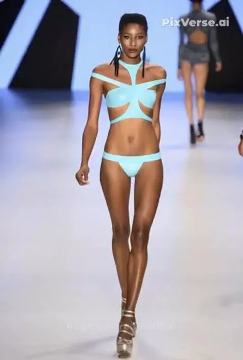Female model with dark skin and hair walks runway in light blue bikini and silver platform heels.