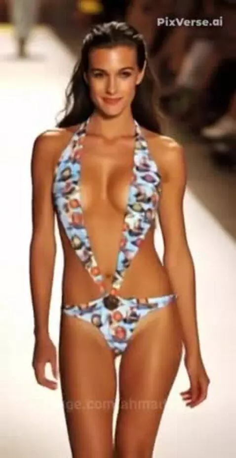 Female model with long dark hair walks runway in abstract blue and orange monokini swimsuit with deep V-neck and side cut-outs.