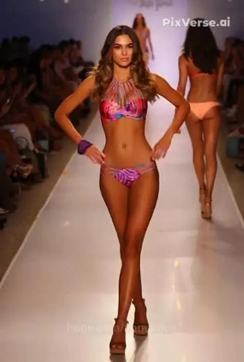 Female model in a colorful abstract-patterned swimsuit confidently walking on a fashion show runway.