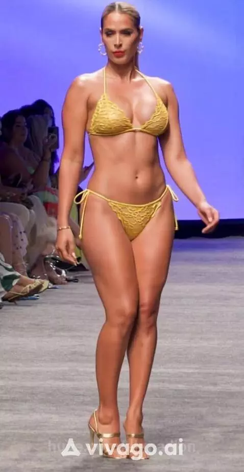 Female model confidently walks a fashion runway in a yellow crochet bikini and high heels.