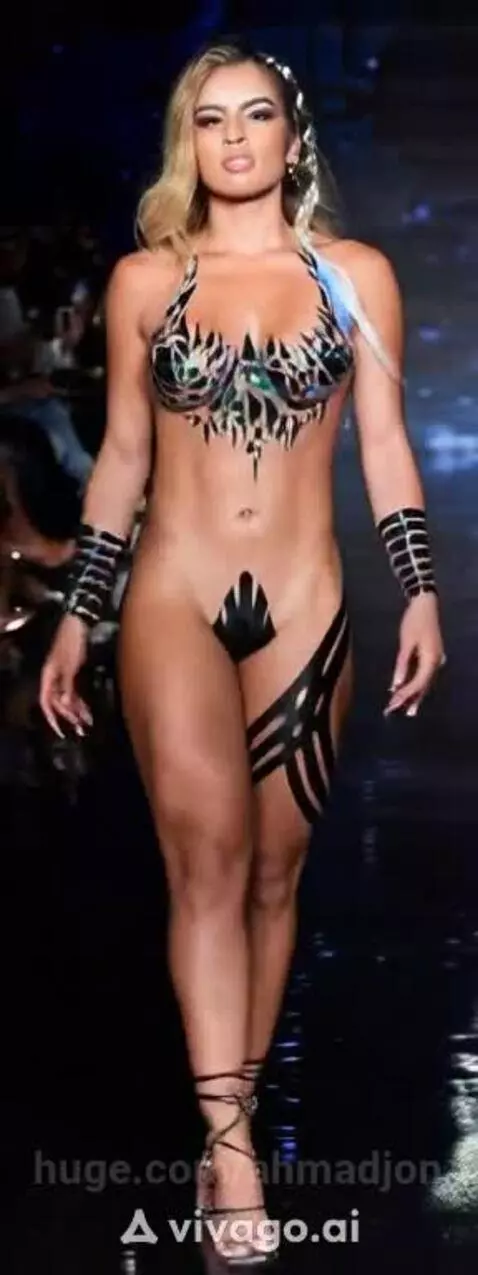 Model with blonde hair walks a catwalk in black body tape and paint, posing confidently.